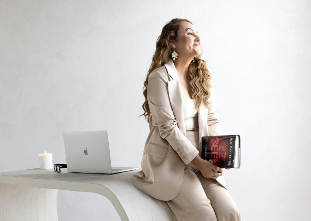 Brand Photographer Tonya Riggs holds Be Seen book by Jen Gottlieb leaning up against desk with computer